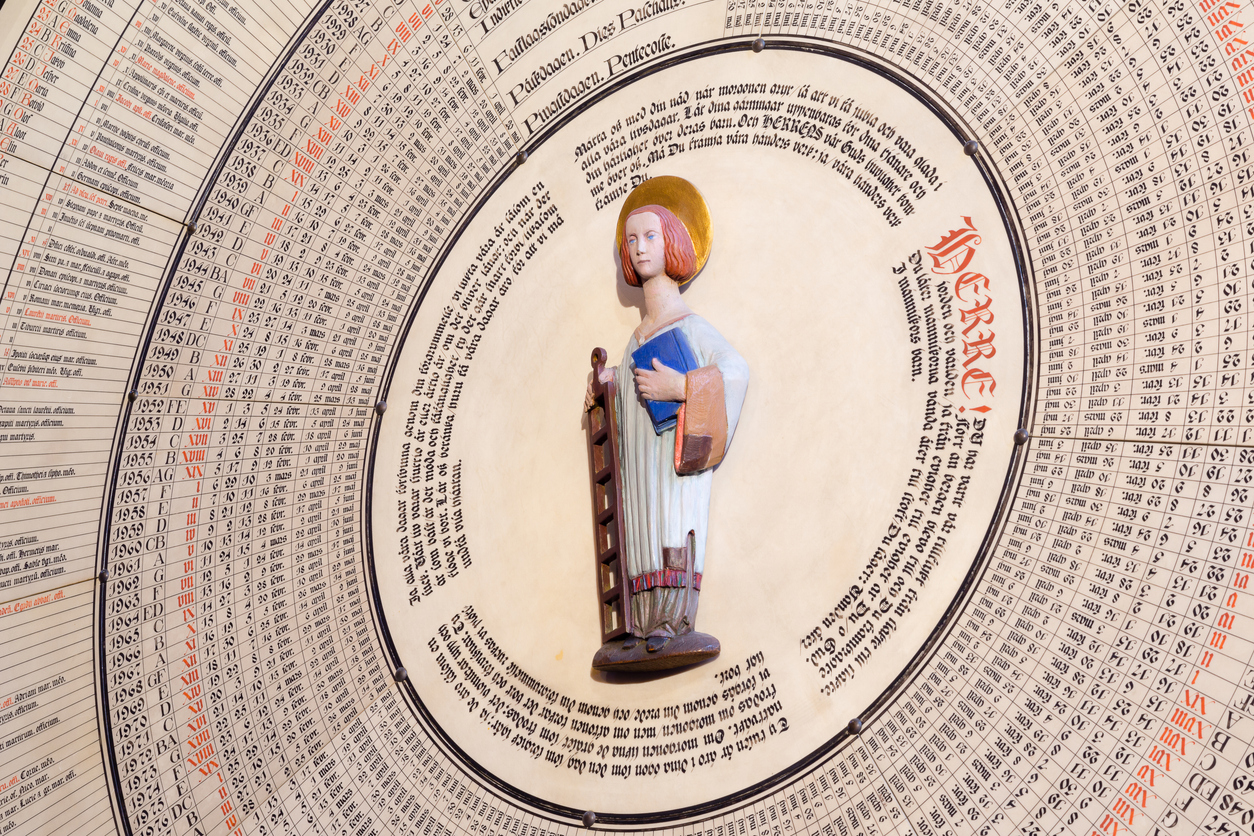 The Saint standing in the center  with a grill and a book in his hands